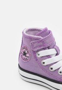 Fialové plátěné vysoké tenisky s bílými tkaničkami, černým logem hvězdy a černou gumovou podrážkou s bílým lemem.