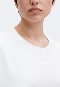 Gros plan sur le bas du visage et le cou d'une personne portant un t-shirt blanc Under Armour à col rond avec un petit logo sur la poitrine.