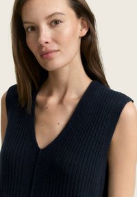 Maritimer ärmelloser Strickpullover in Marineblau mit tiefem V-Ausschnitt, ausgestattet mit einer gerippten Textur und sichtbaren Nahtdetails. Der Stoff wirkt weich und gemütlich.