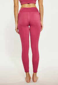Leggings aderenti di un colore rosso bacca uniforme, realizzati in materiale elasticizzato. Presentano un'alta vita e una superficie liscia senza motivi visibili.