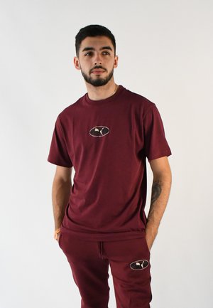 Camiseta color marrón y joggers a juego en una suave mezcla de algodón, con un parche de logo en el pecho y en los joggers, con un ajuste relajado y mangas cortas.