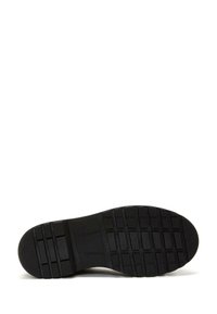 Sole di scarpa in gomma nera con un motivo texture caratterizzato da scanalature e sporgenze. Profilo piatto con elementi di trazione distribuiti uniformemente.