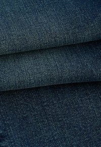 Donker denimstof met een gestructureerde weving. Het oppervlak heeft subtiele variaties in tint en een consistent patroon, gevouwen ter presentatie.