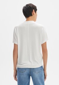 Witte top met korte mouwen van een zachte stof, met een naaddetail op de rug. Gecombineerd met blauwe jeans, wat een ontspannen pasvorm laat zien.