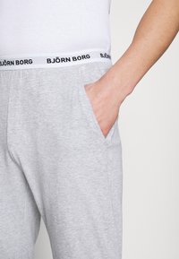Grijze loungebroek met een zachte textuur, voorzien van een witte band met het merk "BJÖRN BORG" in zwart. Inclusief een zijzak.