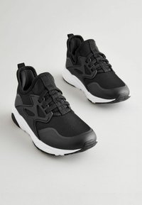 Black athletic shoes with a textured mesh upper, lace-up closure, and white rubber sole. Features a modern design with reinforced accents.