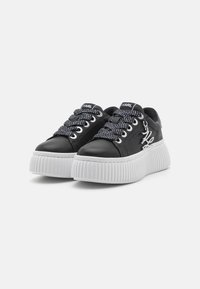 Schwarze Leder-Plateausneaker mit weißer gerippter Sohle, ausgestattet mit schwarz-weißen gemusterten Schnürsenkeln und Logo-Detail an der Zunge.