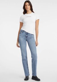 Valge sobiva lõikega T-särk, millel on musta värviga trükitud "GUESS JEANS", kombineeritud helesiniste sirgelõikeliste teksapükste ja mustade pahkluu saabastega.