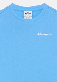 Lys blå bomull T-skjorte med rund hals, med en liten hvit "Champion" logo på venstre brystområde. Jevn tekstur.
