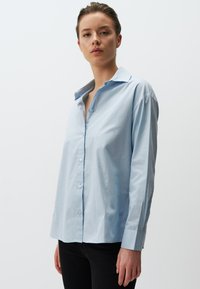 Camicia button-up azzurro chiaro a maniche lunghe in cotone; presenta un colletto classico, pattina centrale con bottoni e una vestibilità rilassata.