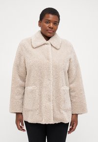Beige, fluffy outerwear jacket with a collar, two front pockets, and a relaxed fit. Soft texture, visible stitching, and cozy appearance.