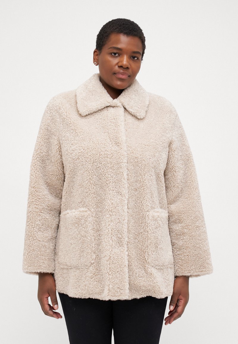 Beige, fluffy outerwear jacket with a collar, two front pockets, and a relaxed fit. Soft texture, visible stitching, and cozy appearance.