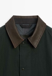 Dark green jacket featuring a brown leather collar, snap closure, and quilted interior. The fabric appears smooth with a matte finish.