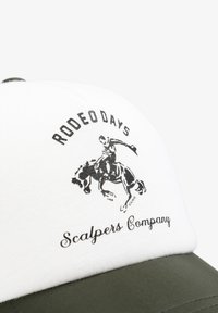 La gorra presenta un panel frontal blanco con el texto "DÍAS DE RODEO" en negro y una silueta de un jinete sobre un caballo. La visera es de color verde oliva.