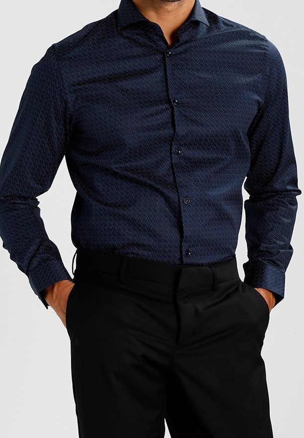 Námořnicky modrá košile na knoflíky s texturovaným vzorem, dlouhými rukávy a klasickým límcem. V kombinaci s černými kalhotami.