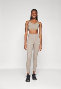 Ensemble de brassière de sport et de leggings beige, avec une texture lisse, une taille haute et un design minimaliste, associé à des chaussures de sport noires.