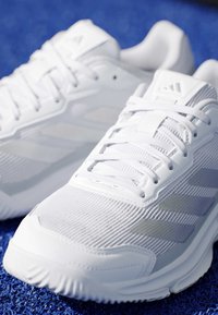 Paire de chaussures de sport blanches avec dessus en mesh et lacets sur une surface bleue texturée.