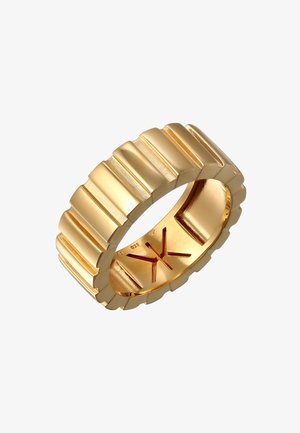 Guldtonet ring med en bred skæft, der har en rillet tekstur og en poleret finish. Indersiden har et indgraveret logo og en glat overflade.