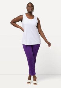Bílý bezrukávový top v kombinaci s purpurovými slim-fit kalhotami. Tkanina se zdá být hladká; top má zaoblený výstřih a kalhoty mají čistou siluetu.
