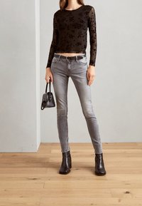 Svart, genomskinlig långärmad topp med blommönster, grå slim fit-jeans och svarta klackiga ankelskor. Liten svart handväska som accessoar.