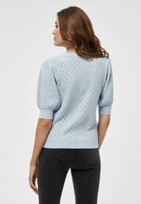 Svetlo modri pleteni pulover z teksturiranim diamantom in napihnjenimi rokavi. Rebrasti manšeti in rob, v kombinaciji s temno sivo jeans hlačami.