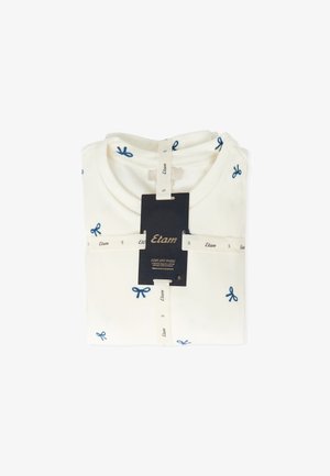 Cremefarbenes T-Shirt mit dunkelblauer Schleifen-Stickerei, ordentlich gefaltet, mit einem Etikett, das den Markennamen und die Größeninformationen enthält.