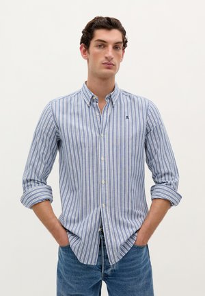 Cotton button-up shirt featuring blue and white vertical stripes, spread collar, and rolled sleeves. Small logo above the chest pocket.