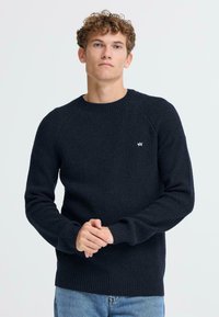 Mornarsko rebrasto pleteno pulover s okroglo izrezom in dolgimi rokavi; vsebuje majhen bel logotip na levem prsnem delu.