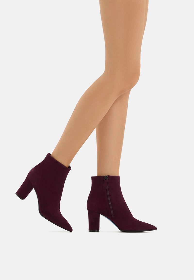 Stivaletti in suede borgogna con punta affusolata e tacco a blocco di altezza media. Presentano una zip laterale per una facile calzata. Texture liscia e morbida.