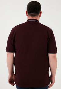 Polo tričko s krátkým rukávem v tmavě burgundské barvě s kontrastním límcem a manžetami. Hladká textura, klasický střih a minimální detaily.