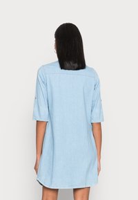 Světlemodré džíny šaty s uvolněným střihem, délka ke kolenům a krátkými rukávy. Má límeček a ohrnuté manžety rukávů. Hladká textura.
