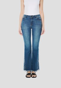 Közép kék mosású, bővülő szárú farmernadrág rojtos szegéllyel és oldalsó virágos hímzéssel. Elöl zsebekkel és gombos záródással rendelkezik.