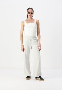 Light gray wide-leg sweatpants and a fitted white tank top, paired with black sneakers featuring white stripes. Simple, casual design.