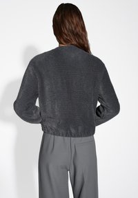 Maglione grigio corto con una finitura morbida e testurizzata; presenta maniche lunghe e una vestibilità rilassata. Abbinato a pantaloni grigi su misura.