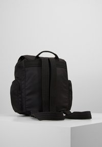 Mochila negra de nailon con dos cremalleras laterales, un asa superior y correas gruesas ajustables, que presenta una textura suave y mate.