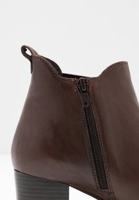 Bottine en cuir marron avec une fermeture éclair sur le côté, col rond, talon en bois foncé cannelé et une languette pour un enfilage facile.