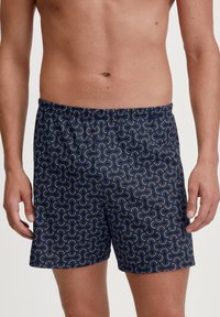 Marinefarbene Schwimmshorts mit einem sich wiederholenden Muster aus bunten, geschwungenen Formen; aus leichtem Stoff mit einem elastischen Bund.
