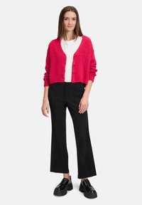 Fuchsia stickad cardigan med knappar, bärs över en vit skjorta; matchad med svarta vida byxor och klumpiga svarta skor. Slät textur.