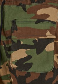 Kamuflage cargo shorts lavet af slidstærkt stof, med en dyb lomme, i grønne, brune og sorte mønstre. Teksturering.
