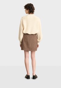 Crème ribbelgebreide trui gecombineerd met een strakke bruine houndstooth minirok. Zwarte schoenen maken de outfit af. Achteraanzicht, effen achtergrond.