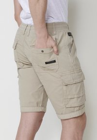 Shorts cargo bej cu un material ușor, dotate cu mai multe buzunare, cu margini răsucite și o bandă elastică confortabilă la talie.