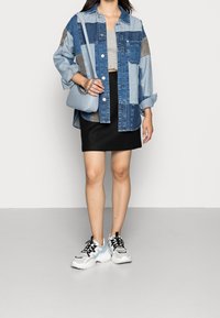 Chemise en denim surdimensionnée avec un design en patchwork dans des tons de bleu et des accents gris, associée à une mini-jupe noire et des baskets blanches épaisses.