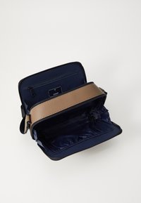 Skórzana torba na ramię z brązowym paskiem i granatowym wnętrzem, wyposażona w kieszeń na suwak i etykietę z logo. Strukturalny design, przestronna komora.
