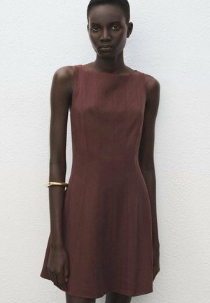 Vestido marrón sin mangas con un cuerpo ajustado y una falda acampanada. Textura suave, diseño minimalista. Pulsera dorada como acento en la muñeca izquierda.