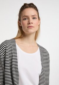 Černobíle pruhovaný cardigan přes jednoduché bílé tričko. Cardigan má volný střih, otevřený přední design a měkkou texturu.