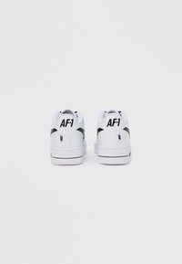 Λευκά αθλητικά παπούτσια Nike Air Force 1 με μαύρες λεπτομέρειες, με υφή στο πίσω μέρος, λείο δερμάτινο πάνω μέρος και λογότυπο στη φτέρνα.
