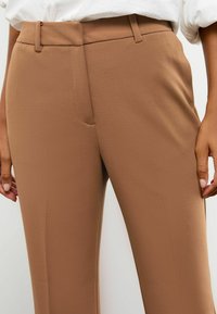 Braune maßgeschneiderte Hose aus einem glatten Stoff, mit flachem Frontdesign, Seitentaschen und Gürtelschlaufen für einen sicheren Sitz.