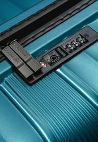 Maleta azul con candado de combinación TSA negro y dos tiradores de cremallera metálicos grabados con "pactastic".
