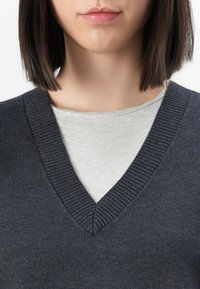 Suéter de cuello en V gris oscuro con cuello acanalado, superpuesto a una camiseta gris claro. Textura suave con detalles de costura sutiles.