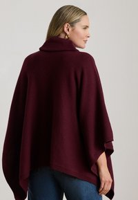 Bordeauxfarvet strikket poncho med høj krave og brede ærmer, med en afslappet pasform og ribkantede kanter. Velegnet til lag-på-lag.